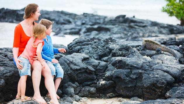 Mother and kids looking at endemic marine iguana at Galapagos islands (photo via shalamov/iStock/Getty Images Plus)