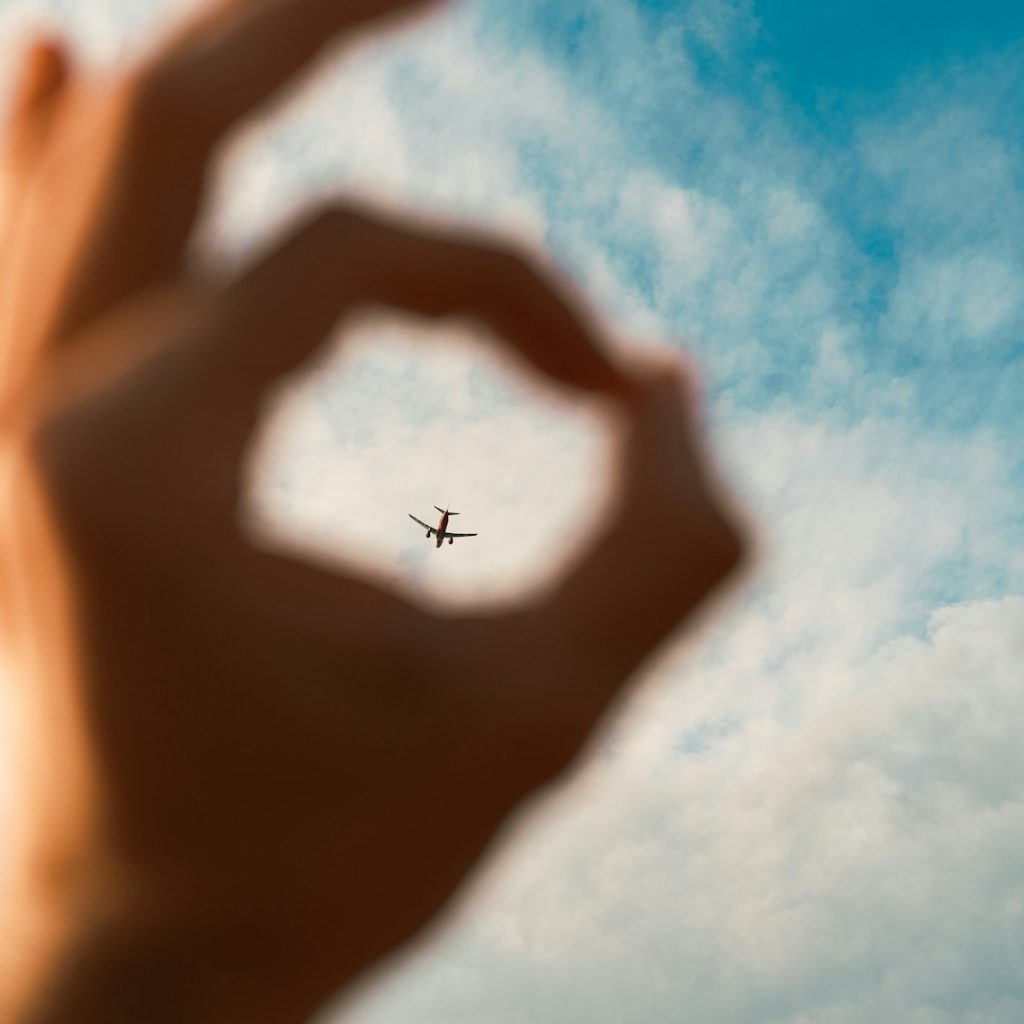 a hand making a heart shape with an airplane in the background