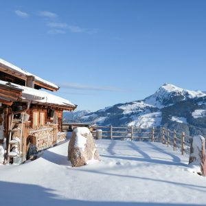a wooden cabin in the snow with mountains in the background