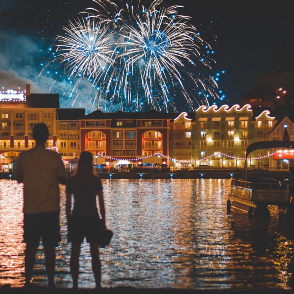 two people standing beside body of water watching fireworks