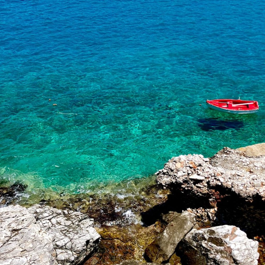 Red fishing boat floating in crystal-clear turquoise water off the rocky coast of Folegandros, Greek Islands